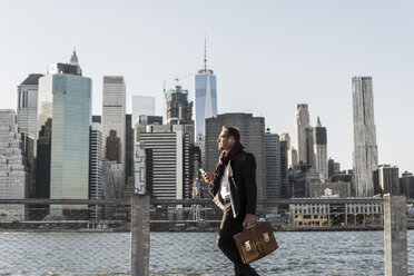 USA, Brooklyn, Geschäftsmann mit Aktentasche vor der Skyline von Manhattan - UUF09286