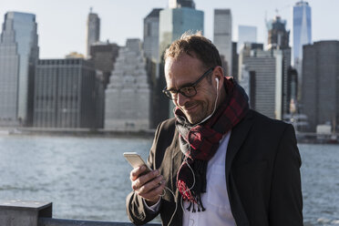 USA, Brooklyn, smiling businessman with earphones looking at his smartphone - UUF09289