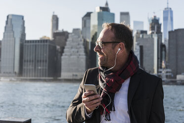 USA, Brooklyn, happy businessman wirh smartphone and earphones - UUF09290