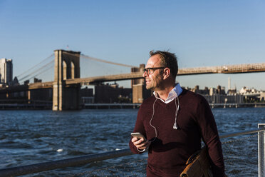 USA, Brooklyn, Geschäftsmann mit Smartphone vor der Brooklyn Bridge - UUF09292