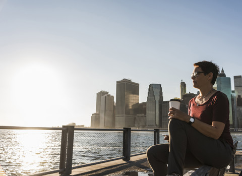 USA, Brooklyn, woman with coffee to go sitting on bench looking at view stock photo