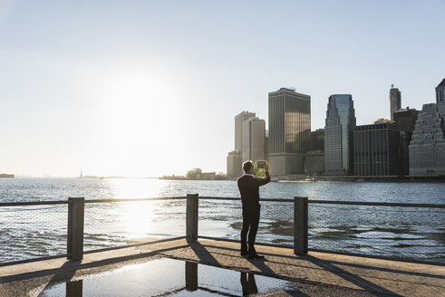 USA, Brooklyn, Rückenansicht eines Mannes, der mit einem Tablet die Skyline von Manhattan fotografiert - UUF09299