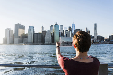 USA, Brooklyn, Rückenansicht einer Frau, die mit einem Tablet die Skyline von Manhattan fotografiert - UUF09300