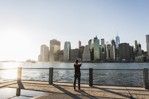 USA, Brooklyn, back view of woman taking picture of Manhattan skyline with tablet stock photo