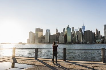 USA, Brooklyn, Rückenansicht einer Frau, die mit einem Tablet die Skyline von Manhattan fotografiert - UUF09302