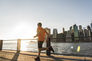 USA, Brooklyn, Mann joggt vor der Skyline von Manhattan am Abend - UUF09307
