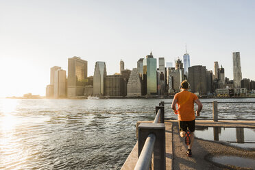 USA, Brooklyn, Rückenansicht eines joggenden Mannes vor der Skyline von Manhattan am Abend - UUF09315