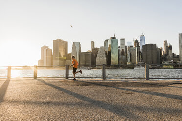 USA, Brooklyn, Mann joggt vor der Skyline von Manhattan am Abend - UUF09317
