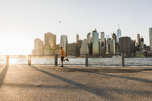 USA, Brooklyn, Mann joggt vor der Skyline von Manhattan am Abend - UUF09317