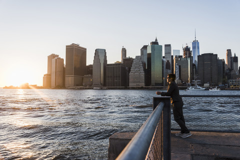 USA, Brooklyn, Frau lehnt sich an ein Geländer und betrachtet die Aussicht am Abend, lizenzfreies Stockfoto