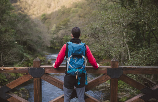 Hiker standing on bridge above a river looking at view - RAEF01562