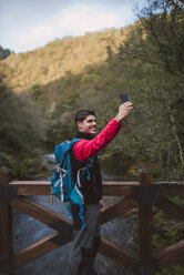 Hiker standing on a bridge taking a selfie - RAEF01564