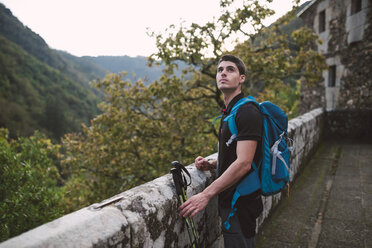 Wanderer steht an einer Steinmauer und schaut sich um - RAEF01572