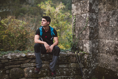 Wanderer rastet sitzend auf einer Steinmauer in der Natur, lizenzfreies Stockfoto