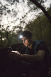 Wanderer mit Stirnlampe im Wald schaut auf Smartphone - RAEF01579