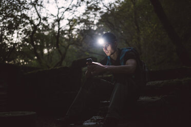 Wanderer mit Stirnlampe im Wald schaut auf Smartphone - RAEF01580