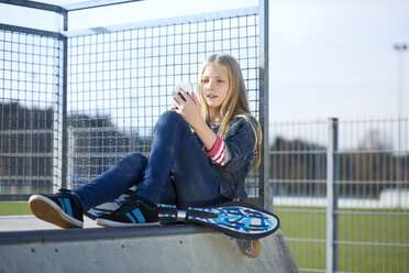 Skateboarder in einem Skatepark schaut auf sein Handy - MAEF12053