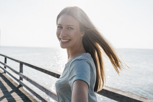 Porträt einer glücklichen jungen Frau auf einem Steg im Gegenlicht - KNSF00667