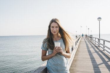 Portrait of happy young woman with coffee to go on jetty - KNSF00672