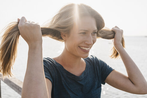 Porträt einer lächelnden jungen Frau mit der Hand im Haar auf einem Steg - KNSF00679