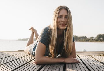 Portrait of happy young woman laying on jetty - KNSF00681