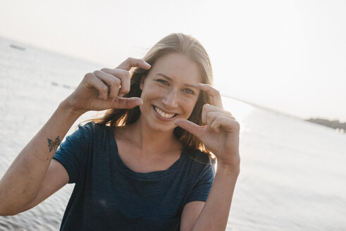 Porträt einer glücklichen jungen Frau, die einen Fingerrahmen formt - KNSF00683