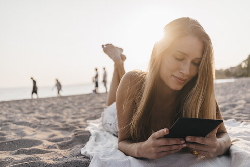 Junge Frau liegt auf einer Decke am Strand und benutzt ein Tablet - KNSF00689