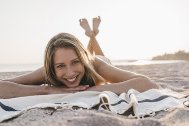 Glückliche junge Frau auf einer Decke am Strand liegend - KNSF00690