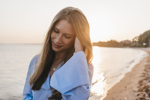 lächelnde junge Frau am Strand bei Sonnenuntergang - KNSF00700