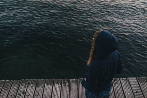 Rückenansicht einer Frau mit Kapuzenjacke, die vor dem Meer steht - KNSF00707