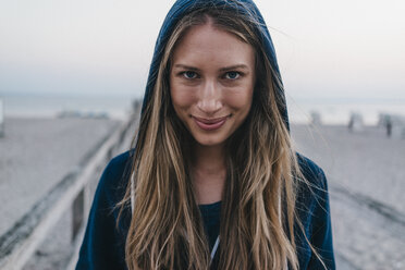 Portrait of smiling young woman wearing hooden jacket standing on jetty - KNSF00710