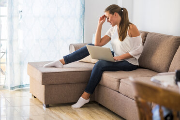 Lächelnde junge Frau sitzt auf der Couch mit Laptop - SIPF01126