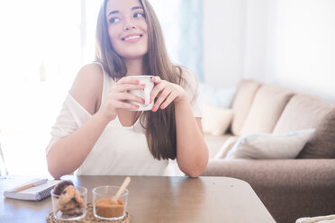 Lächelnde junge Frau trinkt zu Hause Kaffee - SIPF01132