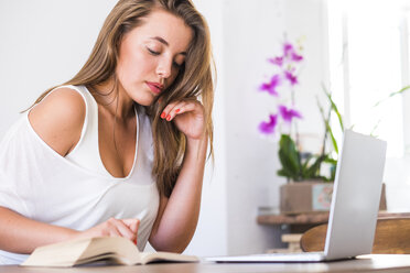 Junge Frau mit Buch und Laptop zu Hause - SIPF01134