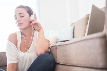 Young woman sitting on the floor of living room listening music with headphones - SIPF01137