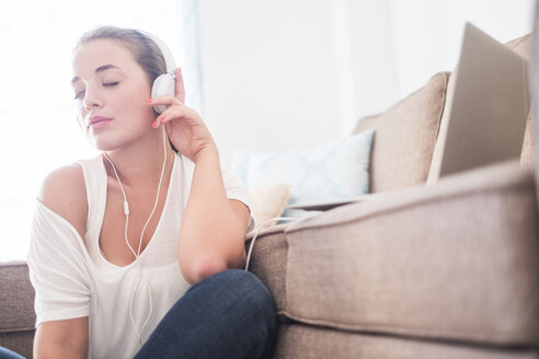 Junge Frau sitzt auf dem Boden des Wohnzimmers und hört Musik mit Kopfhörern - SIPF01137