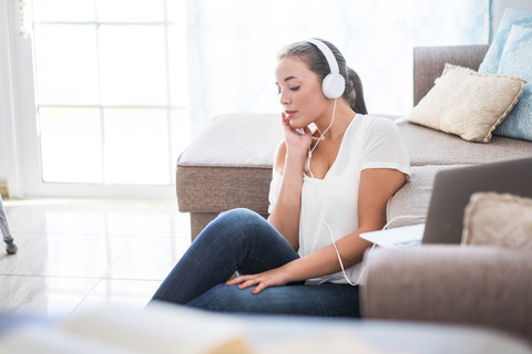 Junge Frau sitzt auf dem Boden des Wohnzimmers und hört Musik mit Kopfhörern, lizenzfreies Stockfoto
