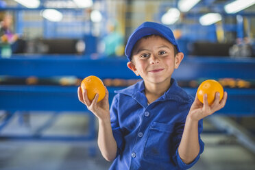 Kleiner Junge im Lagerhaus einer Orangenplantage, der Orangen hält - ZEF11803