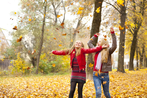 Two happy girls throwing autumn leaves in the air stock photo