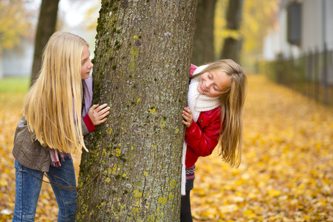 Two girls playing hide and seek in autumn stock photo