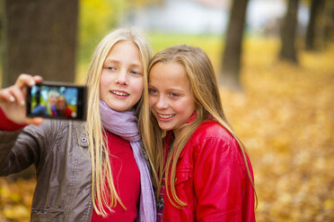 Two smiling girls taking selfie with cell phone in autumn - MAEF12068