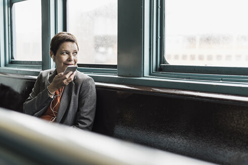 Businesswoman on a ferry with cell phone and earphones - UU09328