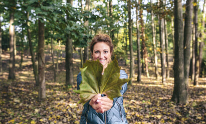 Smiling woman holding autumn leaf in the forest - DAPF00473