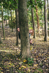 Eltern und kleine Tochter verstecken sich gemeinsam hinter einem Baumstamm - DAPF00475