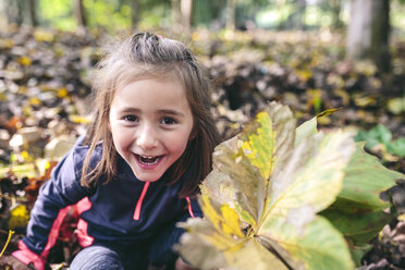 Porträt eines lachenden kleinen Mädchens, das im Wald steht und Herbstblätter hält - DAPF00477