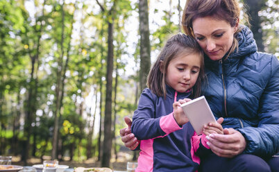 Mutter und kleine Tochter spielen mit Smartphone im Wald - DAPF00489