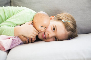 Portrait of smiling little girl lying on couch with her doll - LVF05631