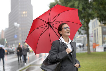 Germany, Berlin, happy businesswoman with red umbrella at Potsdamer Platz - BFRF01790