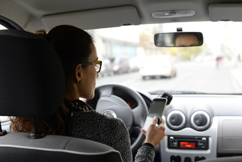 Frau im Auto schaut auf ihr Smartphone - BFRF01793