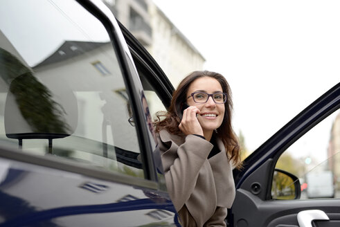 Smiling businesswoman on the phone getting out of car - BFRF01795